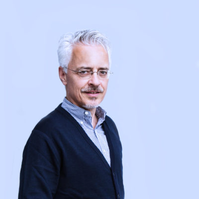 Ein Mann trägt ein kariertes Hemd und darüber einen nachtblauen Cardigan mit V-Ausschnitt.