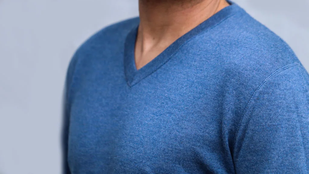 Detailaufnahme vom Brustbereich eines Mannes, der einen jeansfarbenen Pullover mit V-Auschnitt trägt.