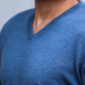 Detailaufnahme vom Brustbereich eines Mannes, der einen jeansfarbenen Pullover mit V-Auschnitt trägt.