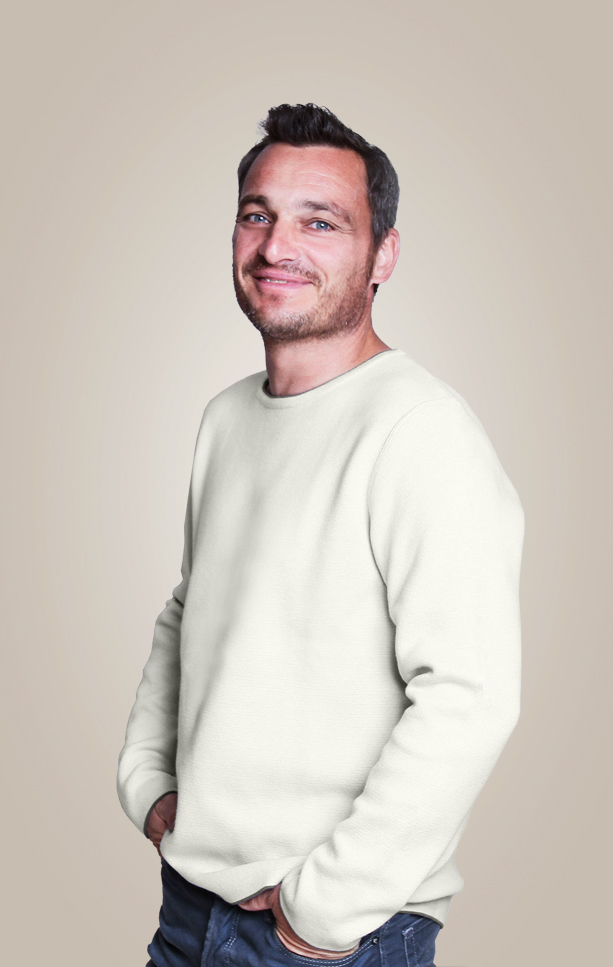 Mann in perl-weissem Pullover steht lässig und lächelt.